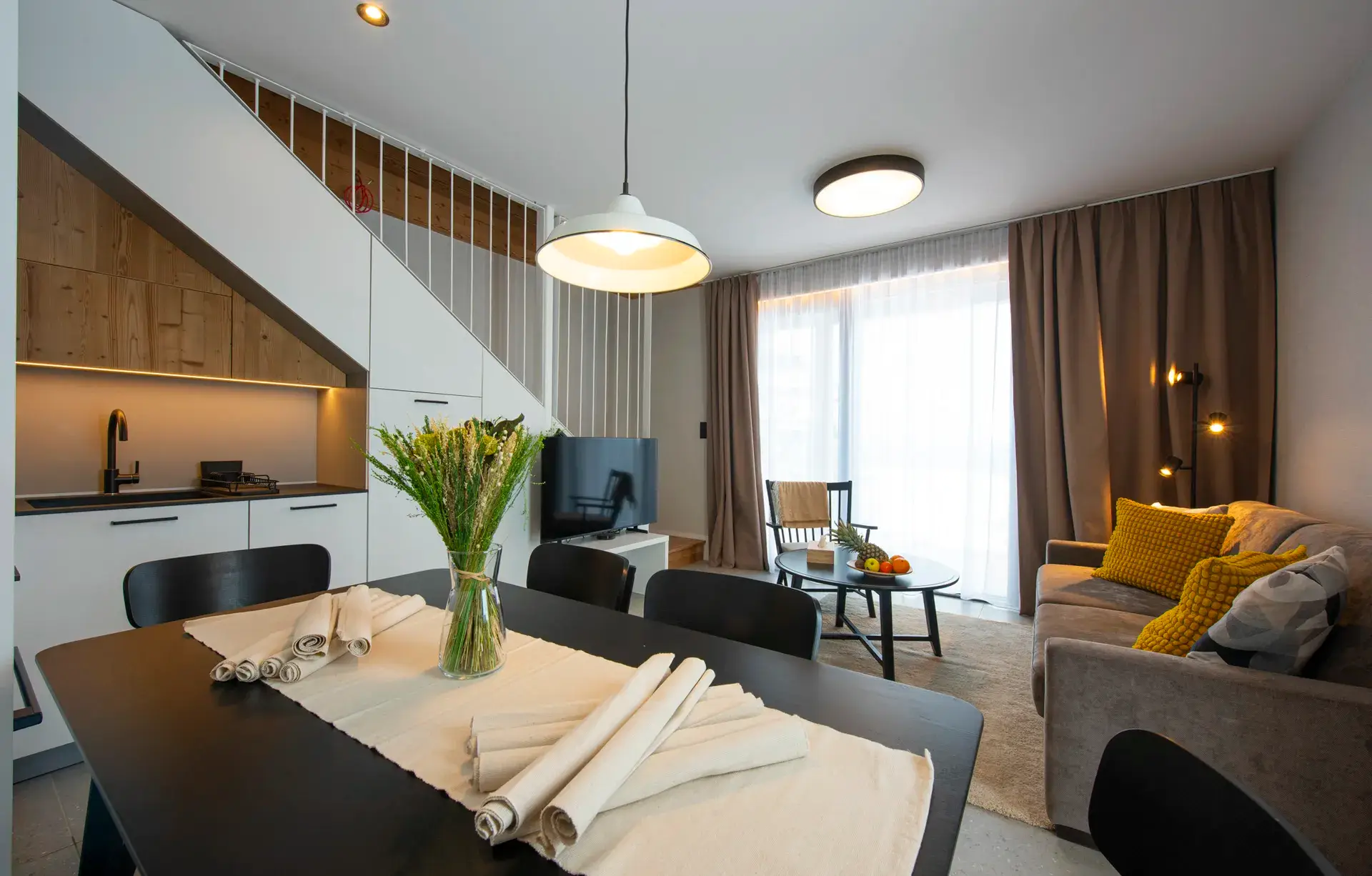 Obývacia časť s jedálenským stolom a schodiskom vo vzorovom mezonete LUXURY