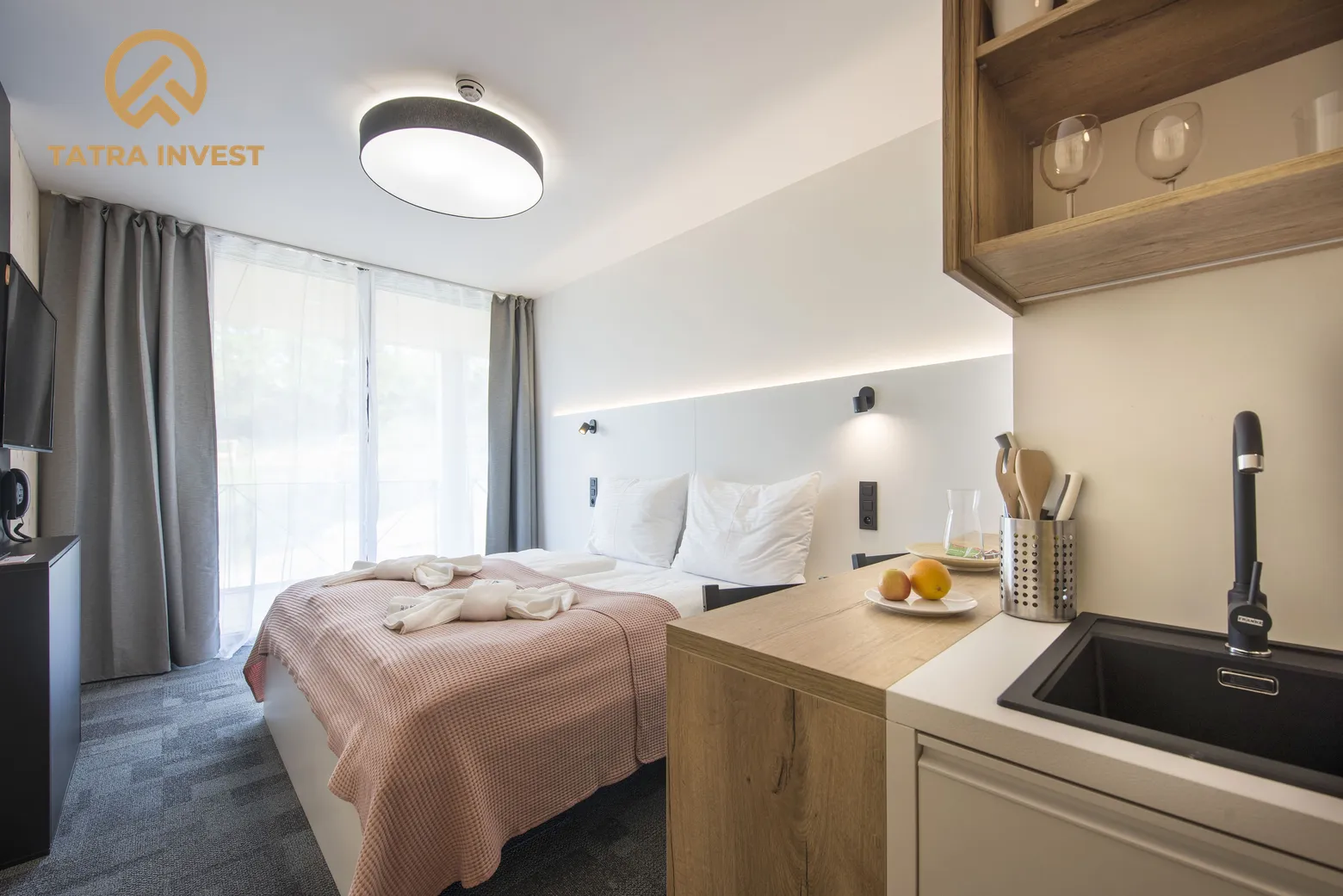 Kuchynský kút s drezom, manželská posteľ a závesmi zakryté dvere na terasu v 1-izbovom apartmáne